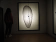 Arturo Álvarez illuminated mesh mask wall sculpture viewed by a person – handcrafted metallic mesh artwork casting a dramatic shadow on the wall